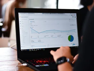 Person analysiert Website-Daten auf einem Laptop mit Google Analytics; sichtbare Diagramme, Statistiken und KPIs zur Performance-Messung