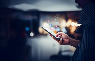 Person tippt auf ein Smartphone, über dem Social-Media-Icons wie Herzchen und Likes schweben – Symbolbild für Interaktion in sozialen Netzwerken