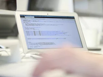 Ein aufgeklappter Laptop mit offenem Quellcode-Fenster zeigt HTML- und CSS-Strukturen für eine Website. Der Fokus liegt auf der Programmieroberfläche, während eine Hand im Vordergrund unscharf zu sehen ist – ein typischer Einblick in die tägliche Arbeit eines Webentwicklers der Denkströme.